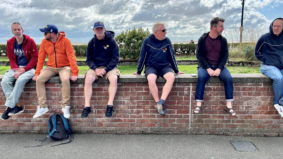 A group of men sitting on a wall

Description automatically generated
